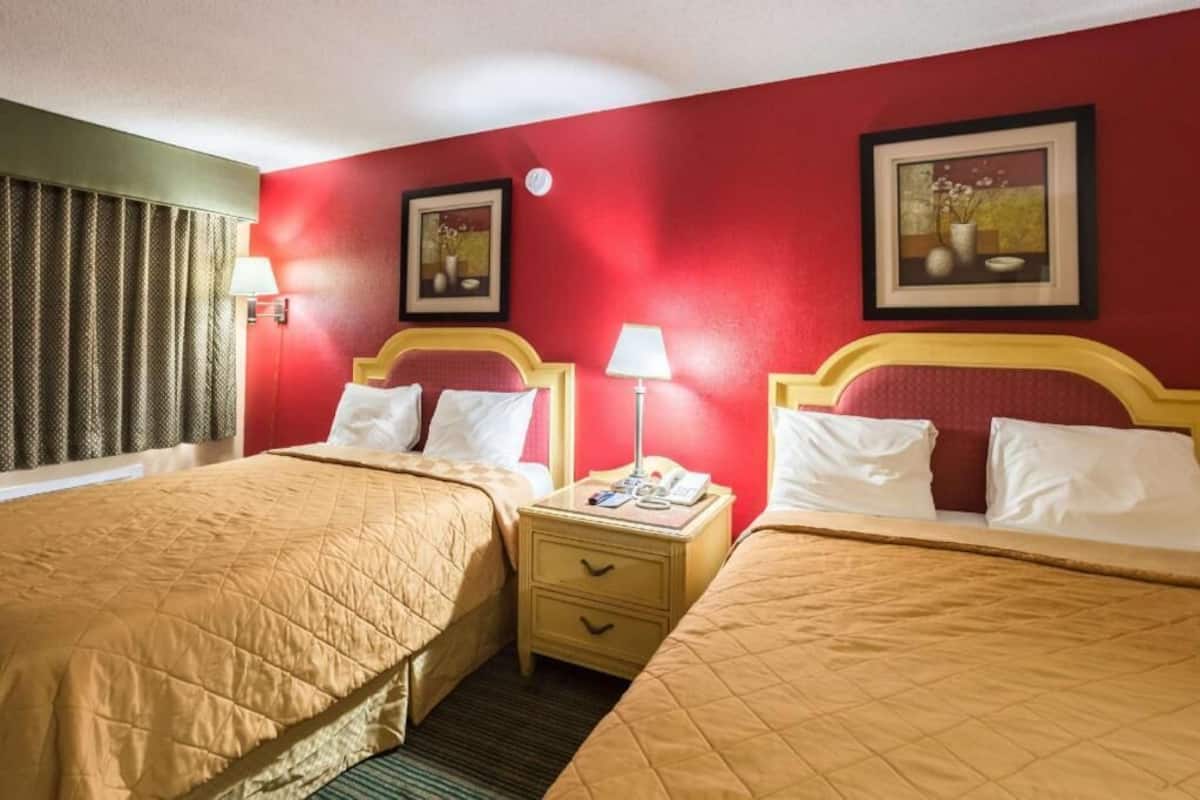 A hotel room with two beds, a nightstand with a lamp, and two framed pictures on the wall.