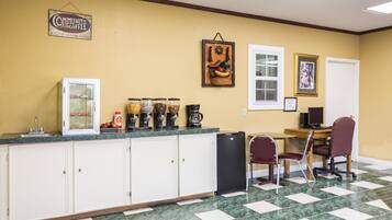 Una cocina con piso de mármol, refrigerador, estación de café y comedor con sillas y mesa.