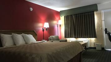 A hotel room with a large bed, two bedside lamps, a desk with a chair, a telephone, and a window with curtains.
