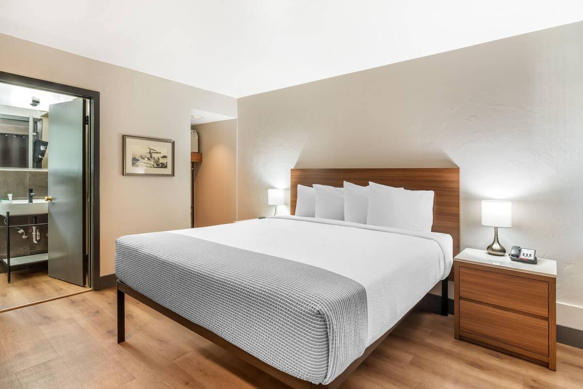 Une chambre d’hôtel avec un lit, des tables de chevet, une armoire et un tableau encadré au mur.