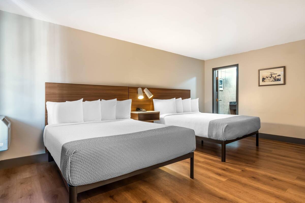 Une chambre d’hôtel avec deux lits, une tête de lit en bois, une table de chevet avec une lampe et un tableau encadré au mur.