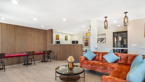 Un área de recepción moderna con un panel de madera, una mesa de recepción, una mesa redonda de vidrio con un jarrón, un sofá rojo y un sillón naranja acolchado.