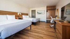 Habitación de hotel con dos camas, un escritorio, una silla, un armario y un espejo.