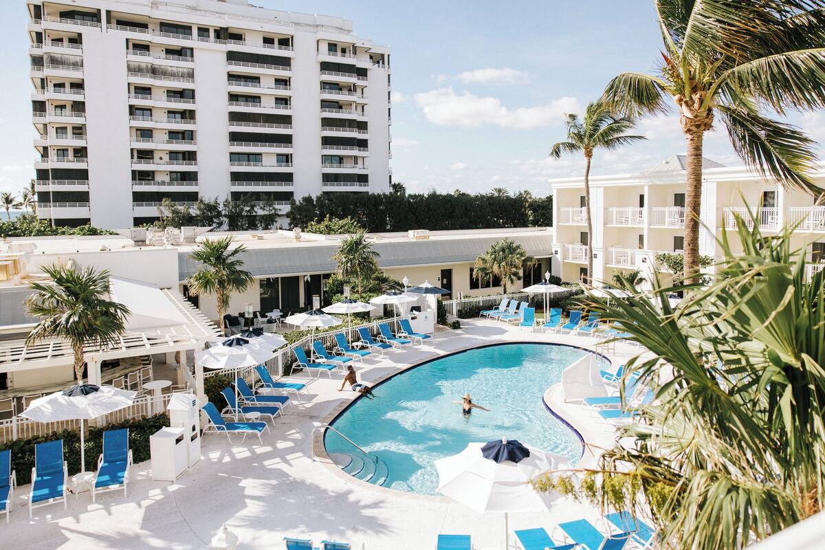 A hotel pool area with blue lounge chairs, umbrellas, and a large building in the background.