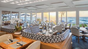 A restaurant with a view of the ocean, featuring wooden tables, cushioned seating, and large windows. - Delray Sands Resort (Highland Beach)