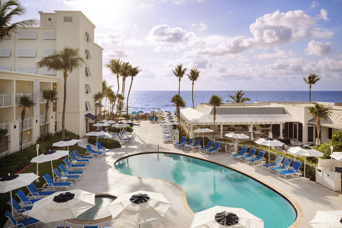 A pool area with lounge chairs and umbrellas, a curved pool, and a view of the ocean.
