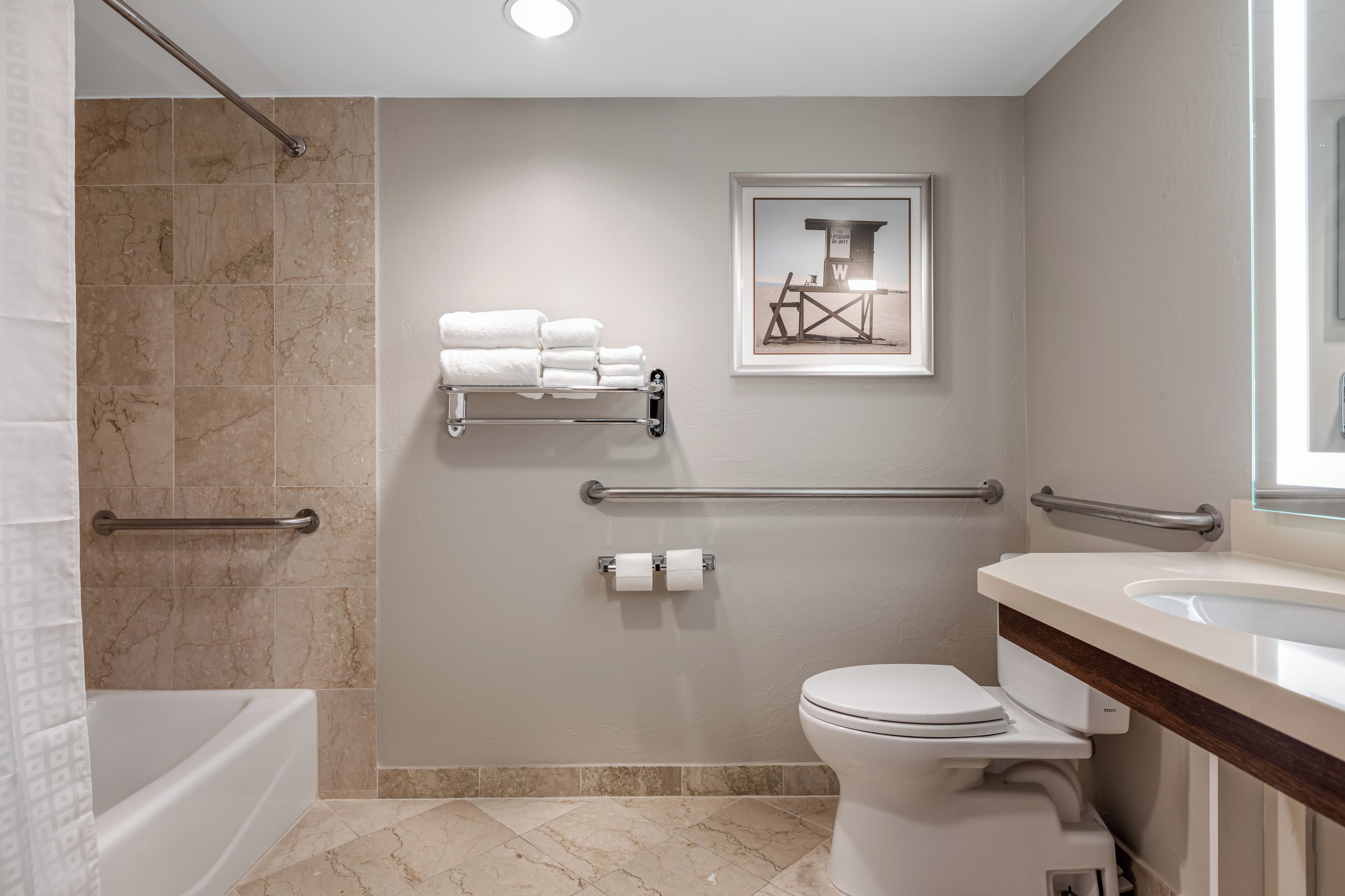 A modern bathroom with a bathtub, toilet, and sink. It includes grab bars and a towel rack.