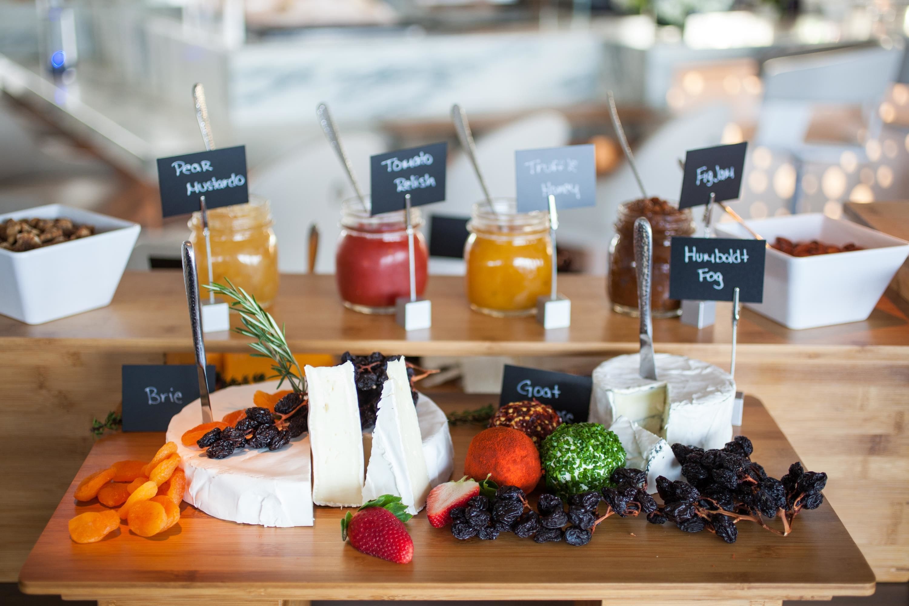 Un plateau de fromages comprenant différents types de fromages et de confitures, chacun étant accompagné d’une étiquette indiquant son nom.