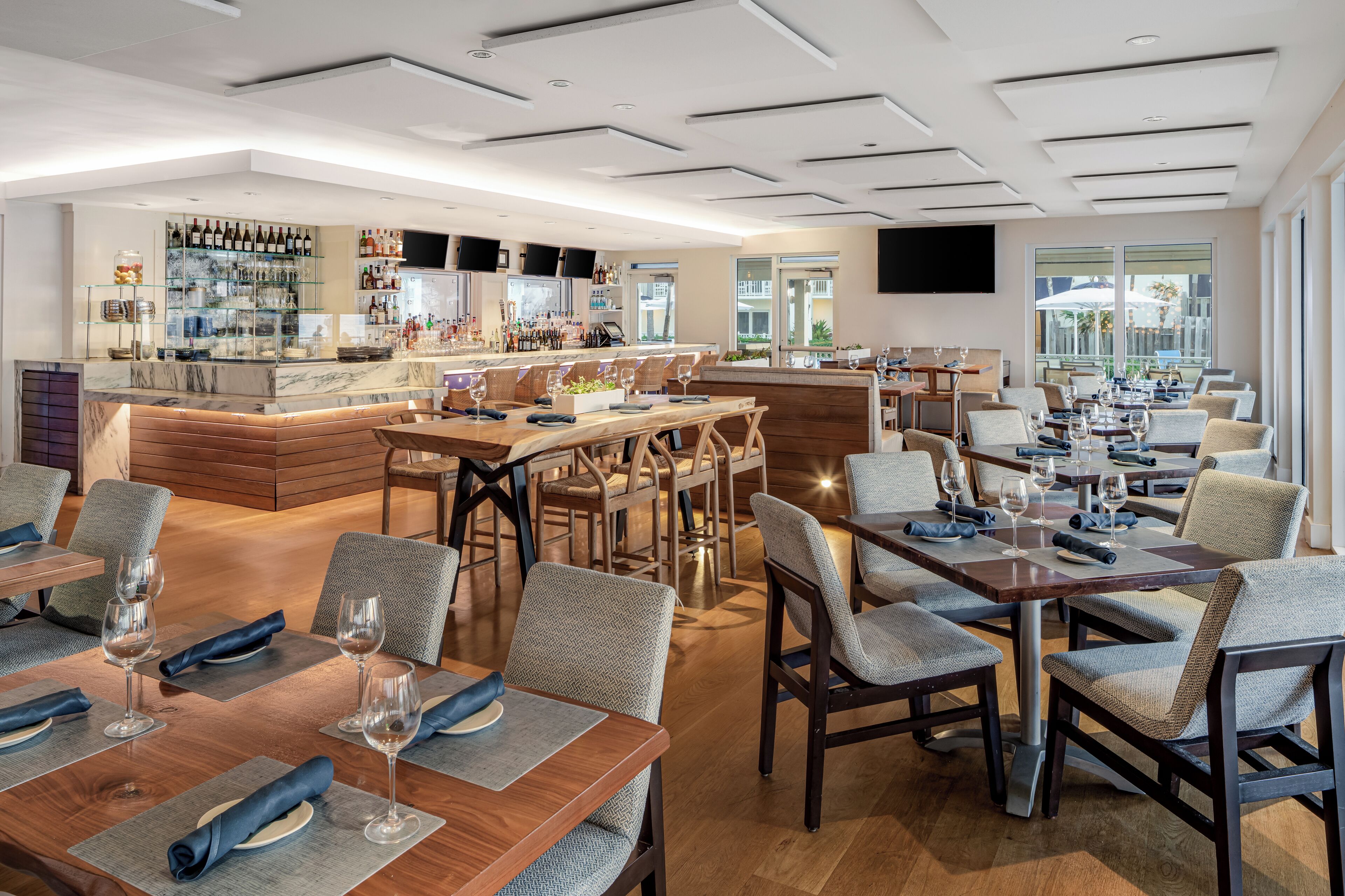 A modern restaurant with multiple dining areas, a bar, and a kitchen visible in the background.