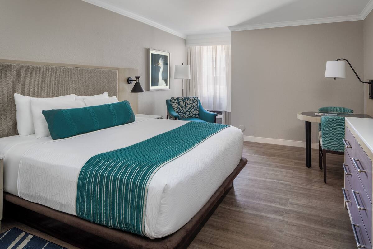 A hotel room with a large bed, a desk, a chair, and a lamp.
