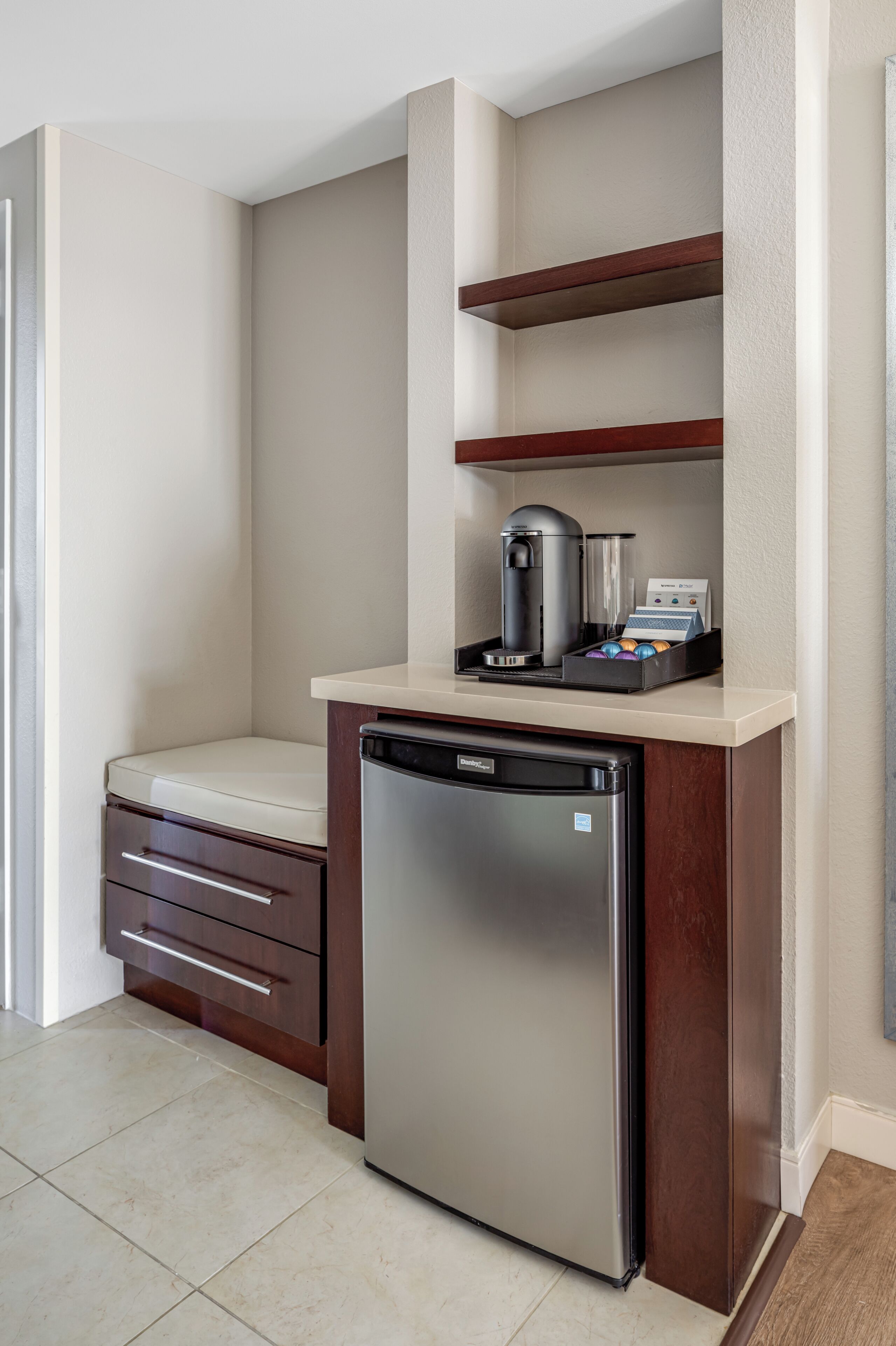 A compact kitchenette with a built-in refrigerator, a coffee machine, and a small countertop.