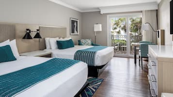 A hotel room with two beds, a desk, and a balcony with a view of palm trees.