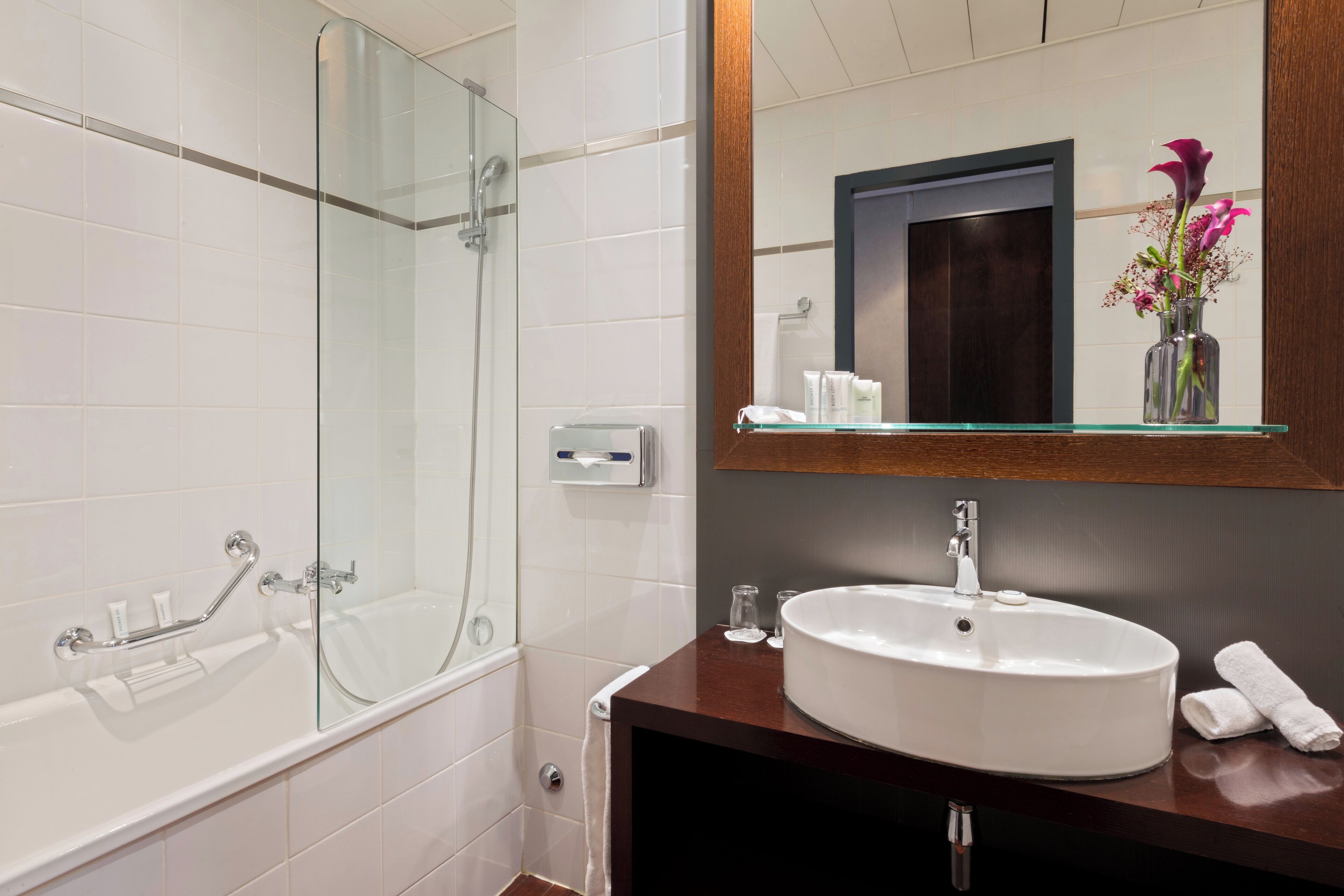 A modern bathroom with a glass-enclosed shower, a white sink, and a wooden vanity.