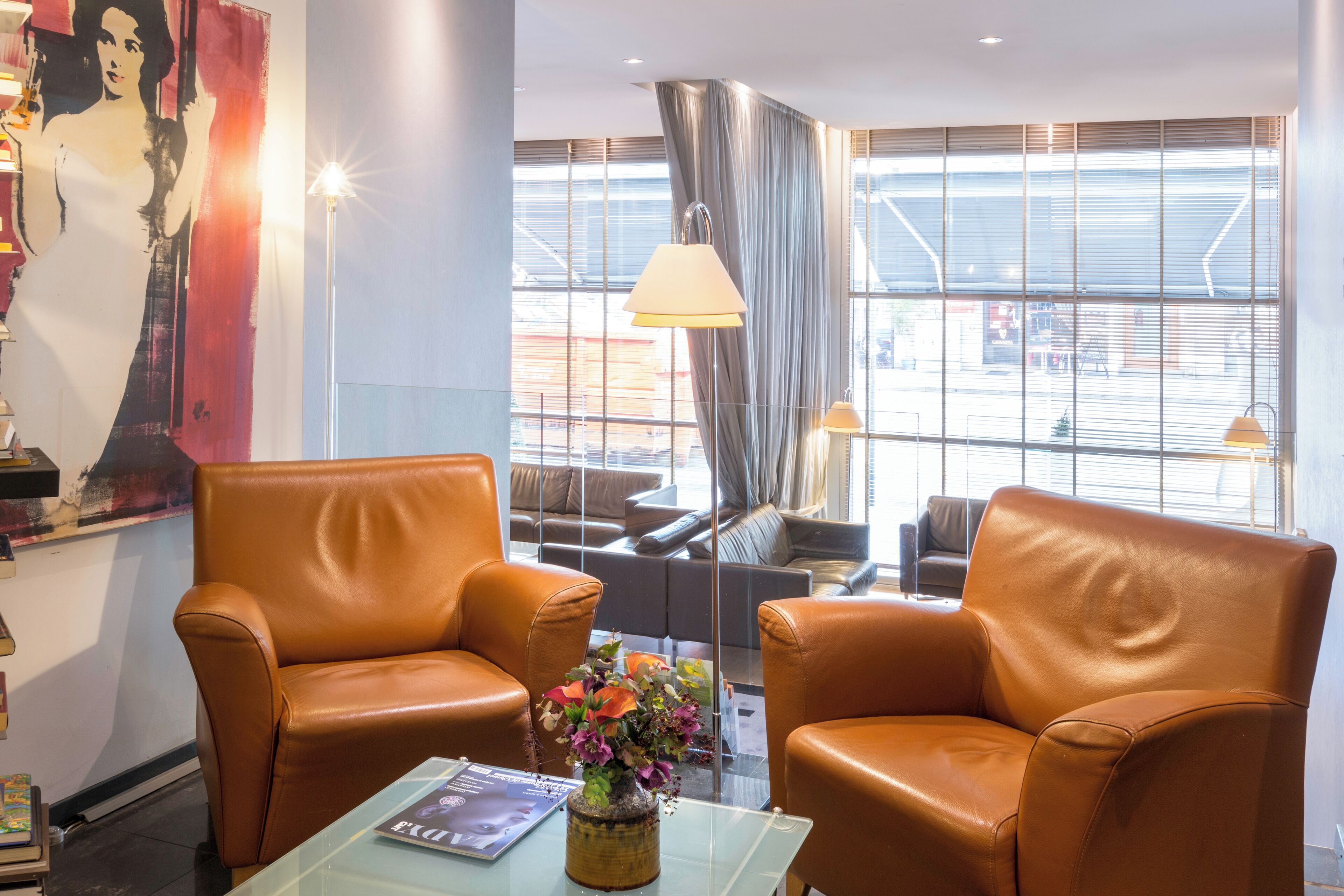 Un'accogliente hall d'hotel moderna, con poltrone in pelle, un tavolino in vetro con una rivista e un'ampia finestra con persiane.