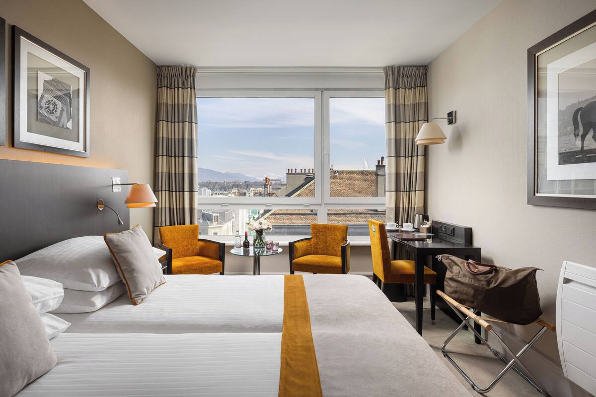 Une chambre d’hôtel avec un grand lit, deux fauteuils, un bureau et une vue sur le paysage urbain.