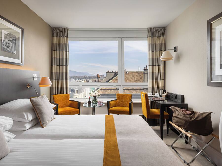Habitación de hotel con una cama grande, dos sillas, un escritorio y vistas a la ciudad.