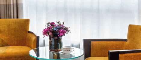 Una habitació amb dues cadires de color mostassa, una taula de vidre amb una tassa blanca i un ram de flors.