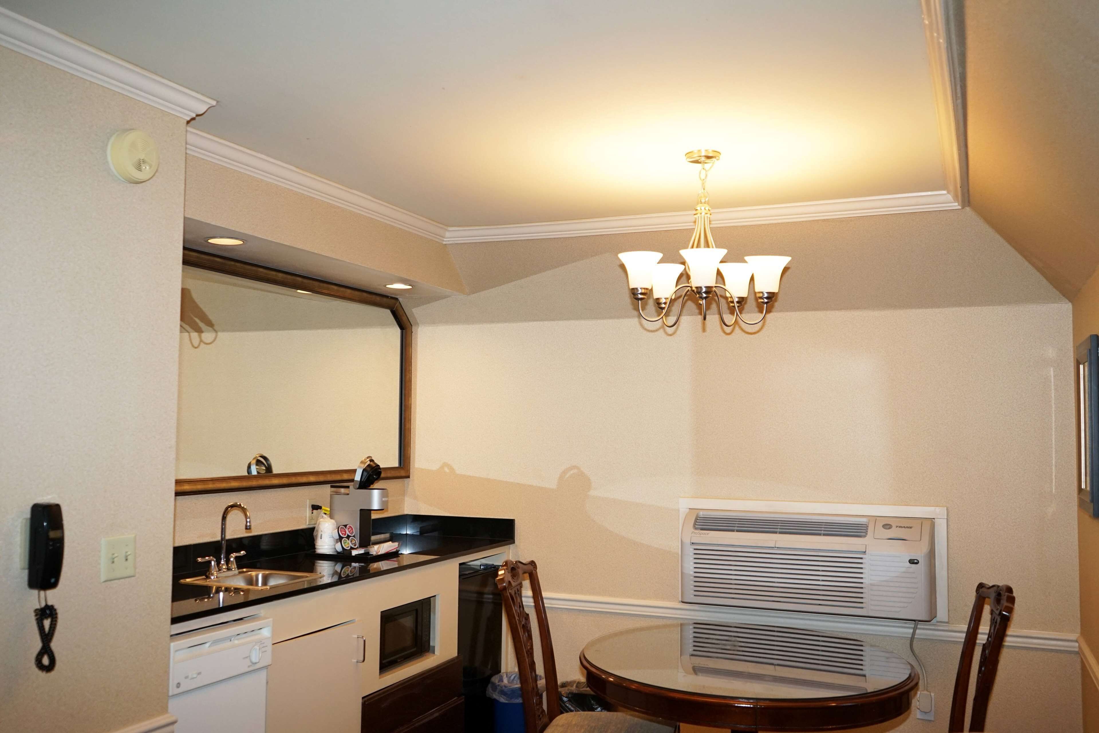 A compact kitchen with a sink, stove, and microwave, a dining table with chairs, a chandelier, and an air conditioning unit.