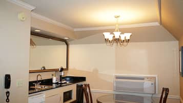 Cocina compacta con pileta, estufa y microondas, una mesa de comedor con sillas, un candelabro y un equipo de aire acondicionado.