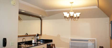 A compact kitchen with a sink, stove, and microwave, a dining table with chairs, a chandelier, and an air conditioning unit.