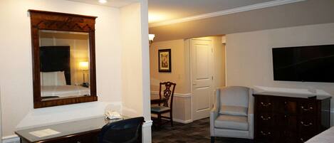 A hotel room with a desk, chair, dresser, and a television.