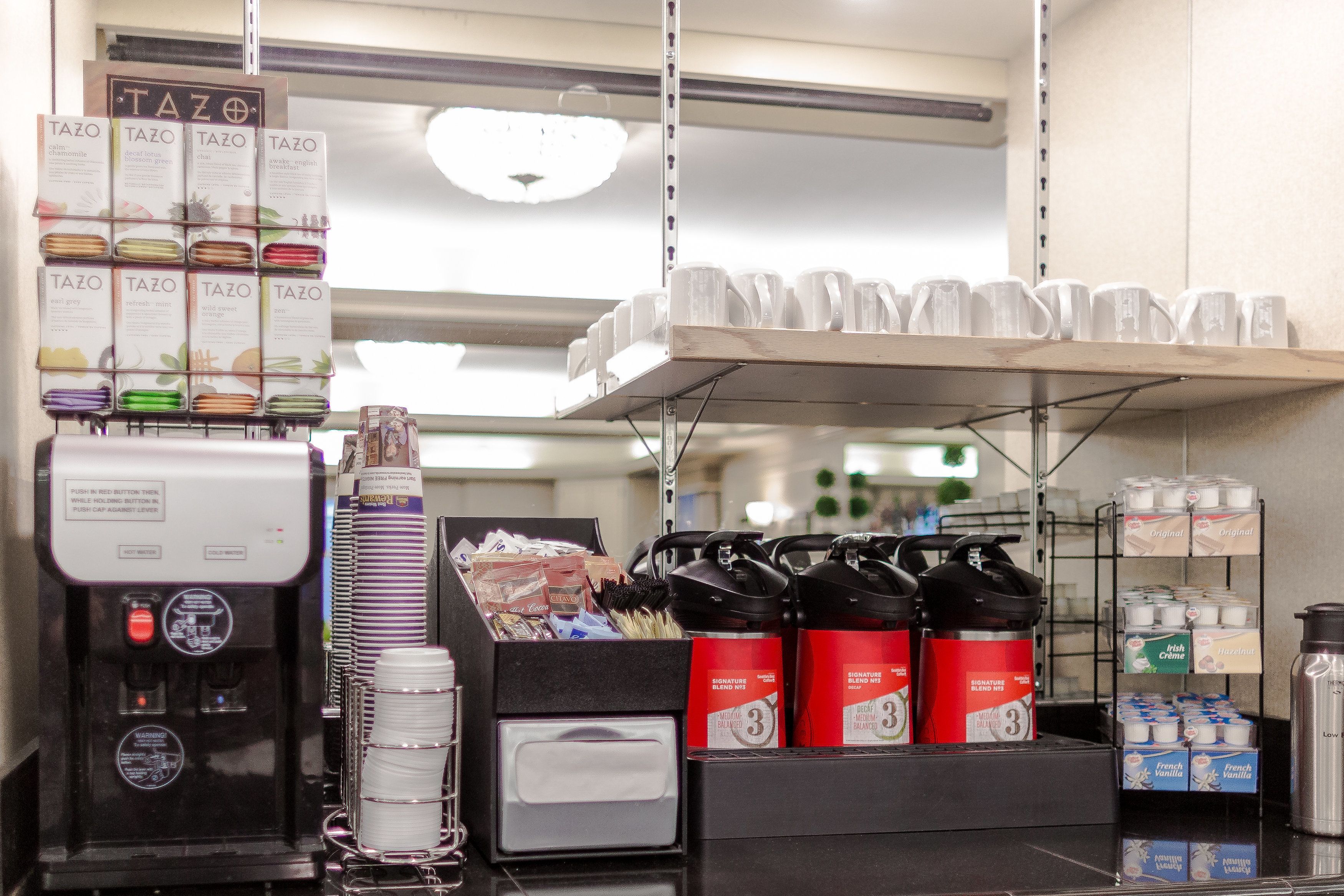 Una estación de café con varios dispensadores, una pila de vasos desechables y una variedad de cápsulas de café.