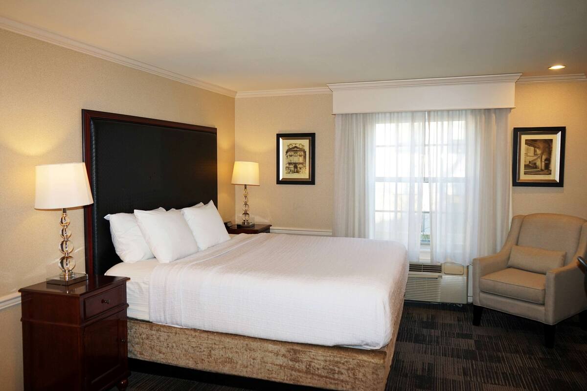 A hotel room with a large bed, two bedside tables with lamps, a chair, and a window with curtains.