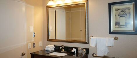 Une salle de bain avec un grand miroir, un lavabo avec un meuble-vasque, un porte-serviettes et un tableau encadré au mur.