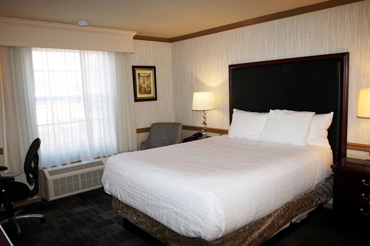 A hotel room with a large bed, a desk with a chair, a desk lamp, and a framed picture on the wall.