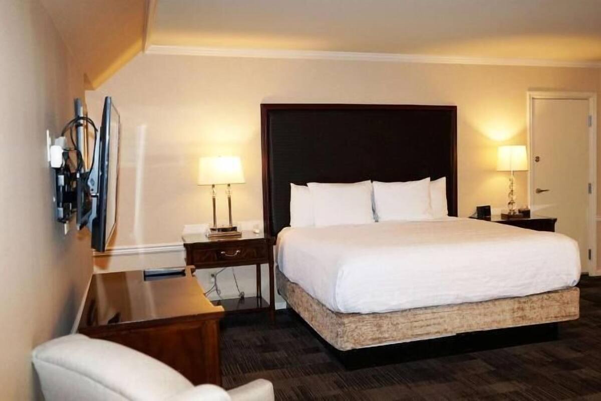 A hotel room with a large bed, two bedside tables with lamps, a desk, and a chair.