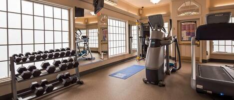 A gym with exercise equipment, a treadmill, and a rack of dumbbells.