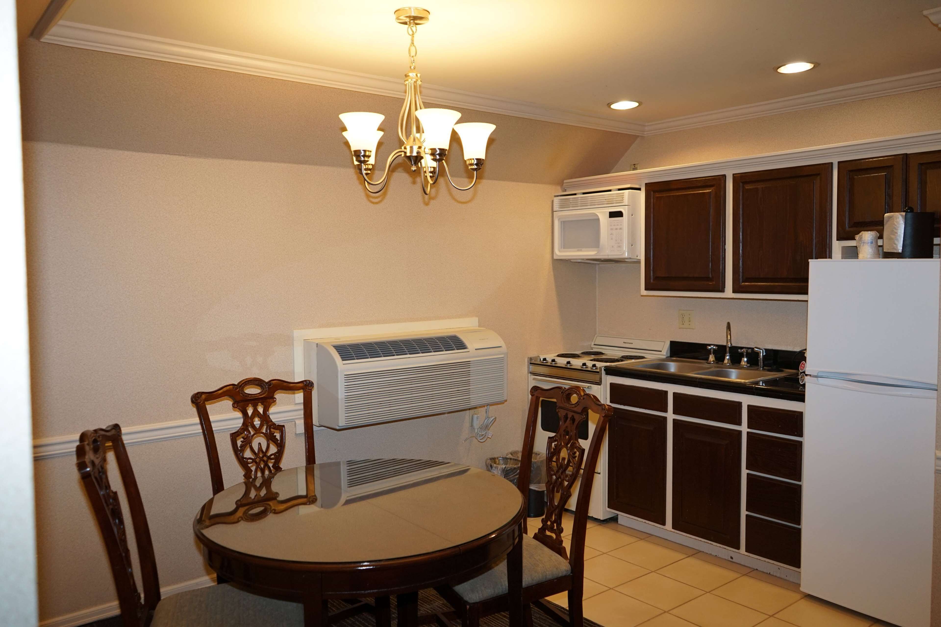 A compact kitchen with a dining table, chairs, a chandelier, a microwave, stove, and cabinets.