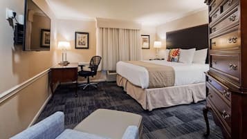 Habitación de hotel con cama, escritorio, silla, cómoda y un espejo grande.