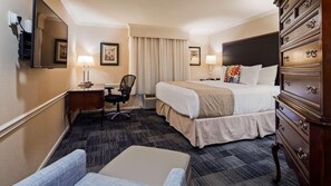 A hotel room with a bed, desk, chair, dresser, and a large mirror.