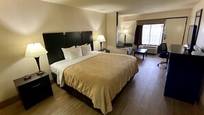 A hotel room with a bed, bedside tables, a desk, a chair, a mirror, and a TV. - Quality Inn & Suites Orlando Airport (Orlando)