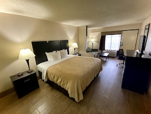 Una camera d'albergo con un letto, comodini, una scrivania, una sedia, uno specchio e una televisione.