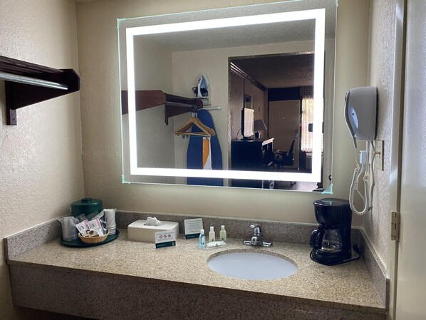 A hotel bathroom with a granite countertop, a white sink, a mirror with a light, a hairdryer, and a coffee maker. - Quality Inn & Suites Orlando Airport (Orlando)