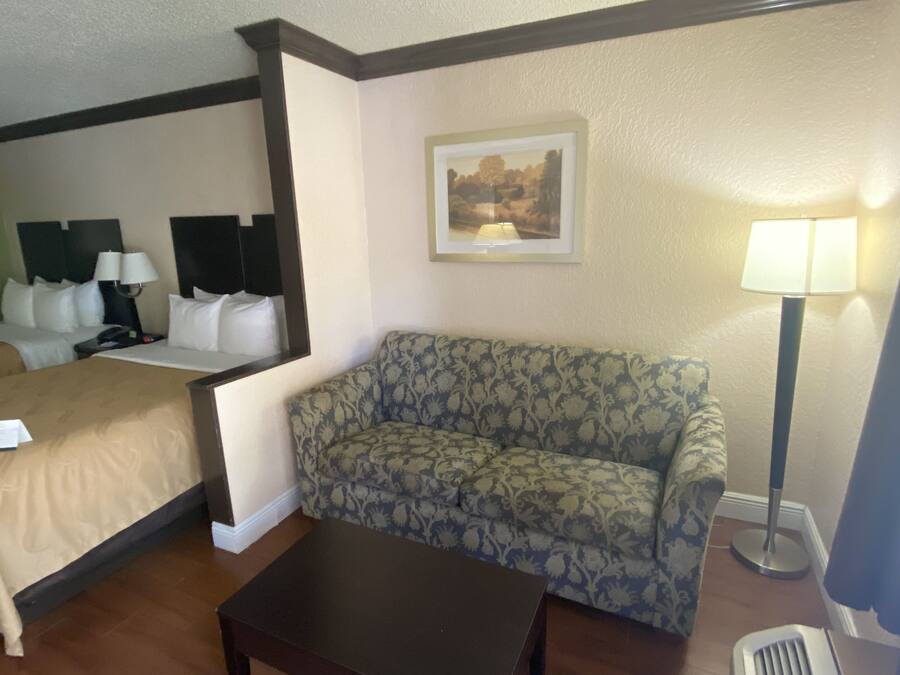 A hotel room with a bed, a sofa, a coffee table, a lamp, and a picture on the wall.