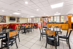 A restaurant with multiple tables and chairs, a kitchen area, and a ceiling with recessed lighting. - Quality Inn & Suites Orlando Airport (Orlando)