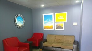 Quarto com sofá de couro marrom, duas poltronas vermelhas e uma pequena mesa. Há três quadros na parede.