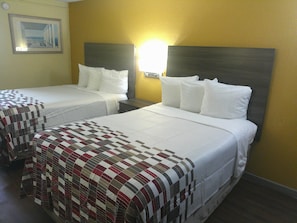 A hotel room with two single beds, each with white bedding and a headboard. There is a wall-mounted light fixture above the beds, and a framed picture on the wall to the left. - Red Roof Inn Hampton Coliseum (Hampton)