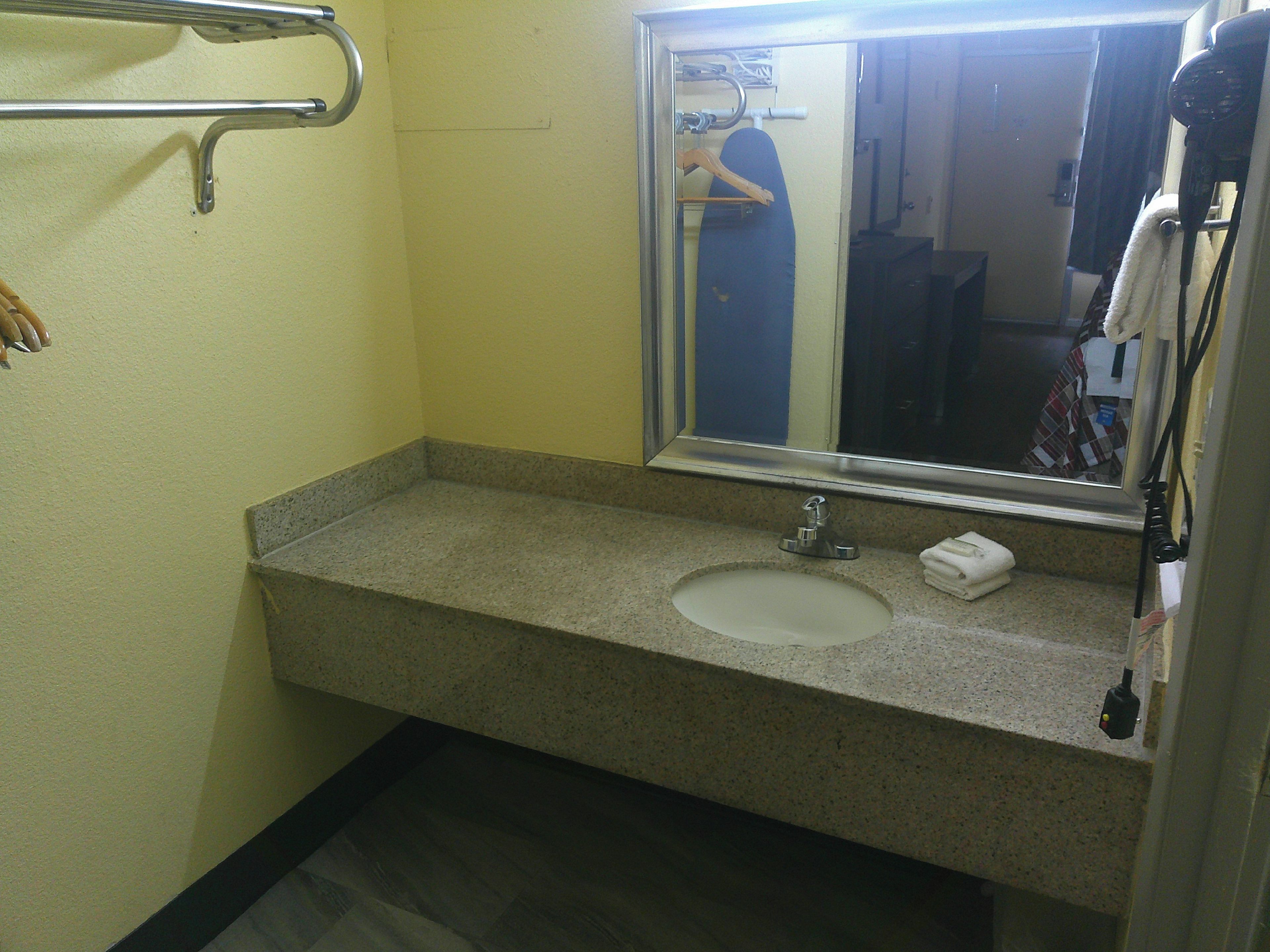 Un baño con encimera de granito, lavamanos, espejo y toallero.