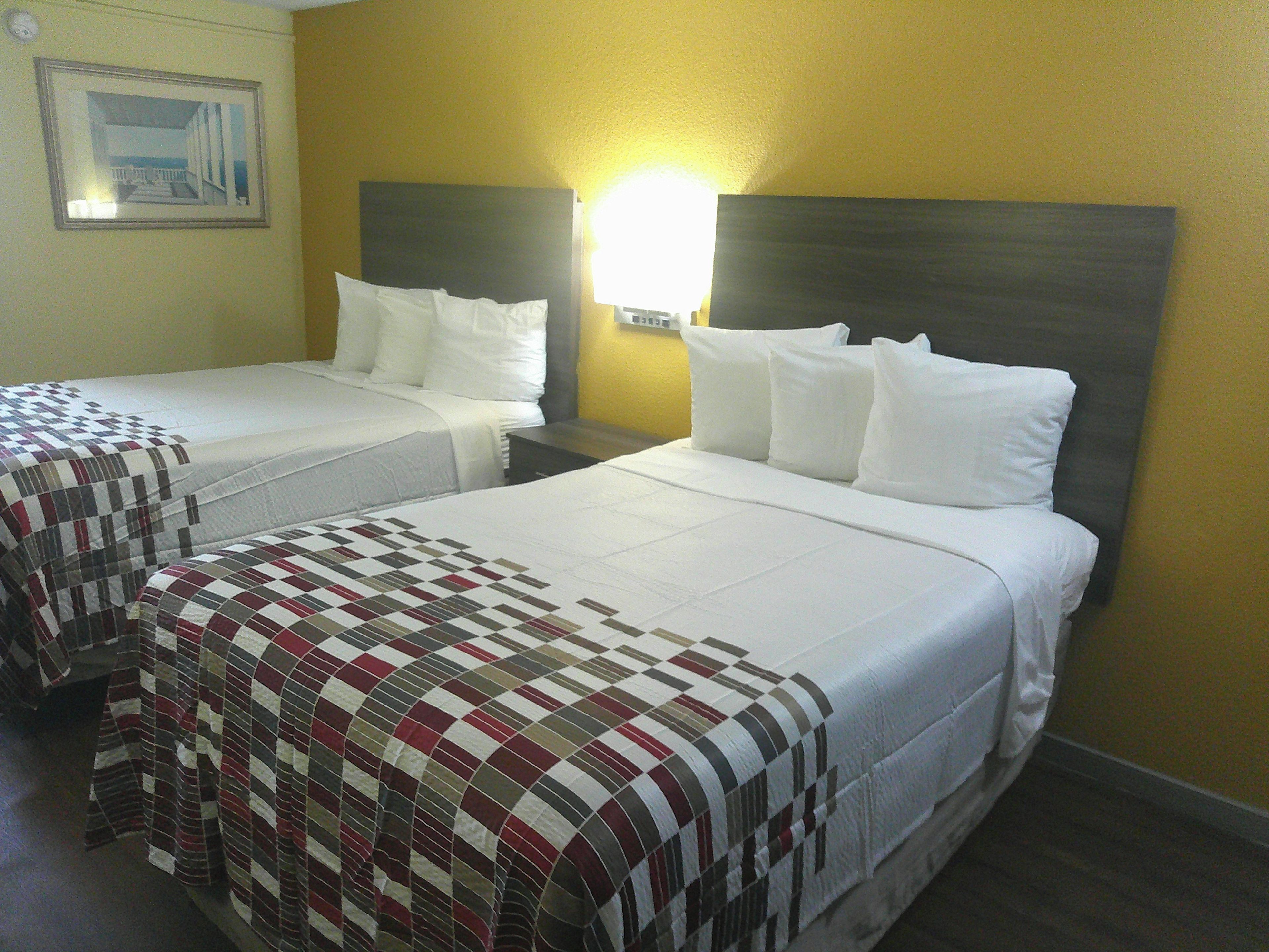 A hotel room with two beds, a nightstand, and a wall-mounted lamp.