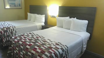 A hotel room with two beds, a nightstand, and a wall-mounted lamp.