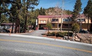 A two-story building with a red roof, a sign for a restaurant, and a paved driveway leading to the entrance. - Rodeway Inn Wildwood Inn (Mammoth Lakes)