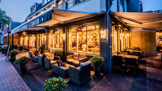 Un restaurante con terraza, mobiliario de mimbre y un letrero que dice 'DINER'.