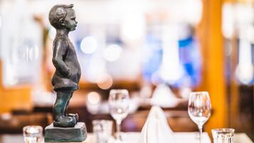 Uma mesa de jantar posta com uma estátua de criança, taças de vinho e talheres.
