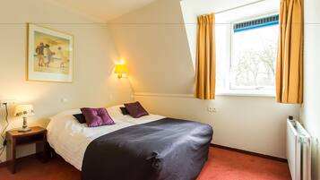 A hotel room with a bed, a nightstand, a lamp, a window with curtains, and a painting on the wall.