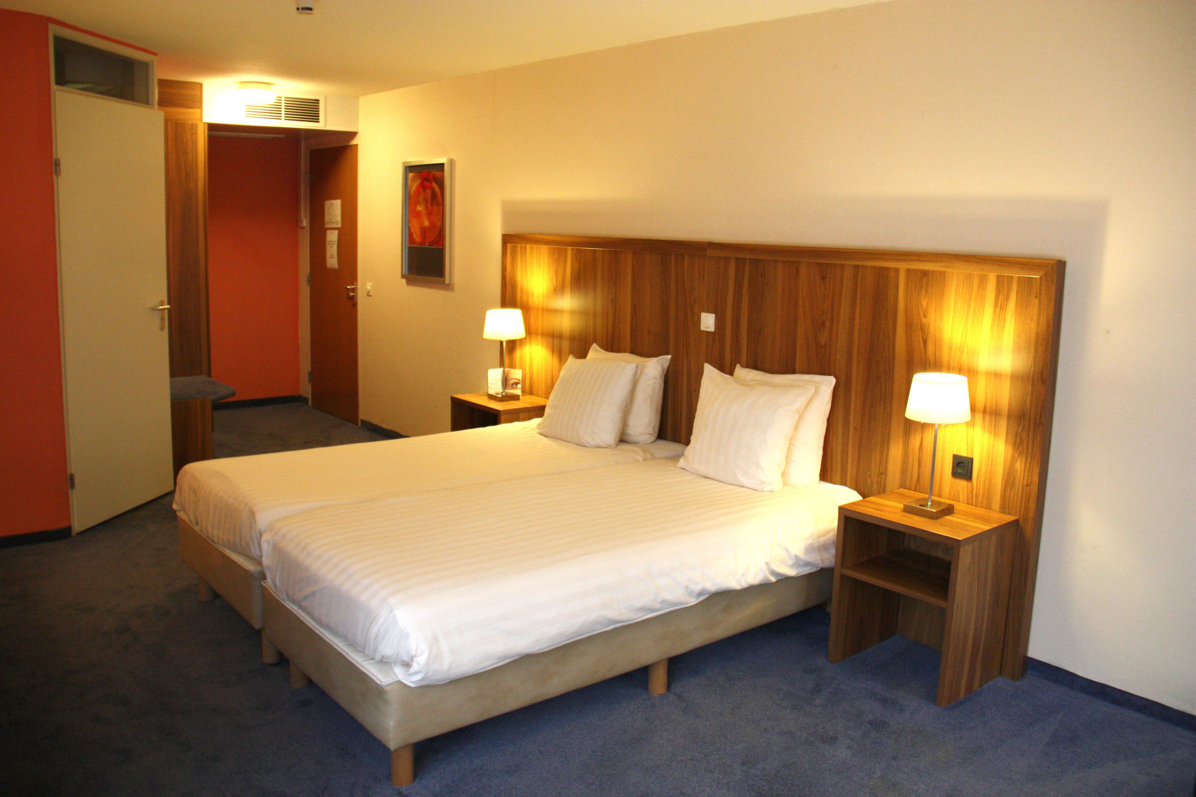 Quarto de hotel com uma cama grande, duas mesas de cabeceira com luminárias, uma cabeceira de madeira e uma porta que dá para um banheiro.