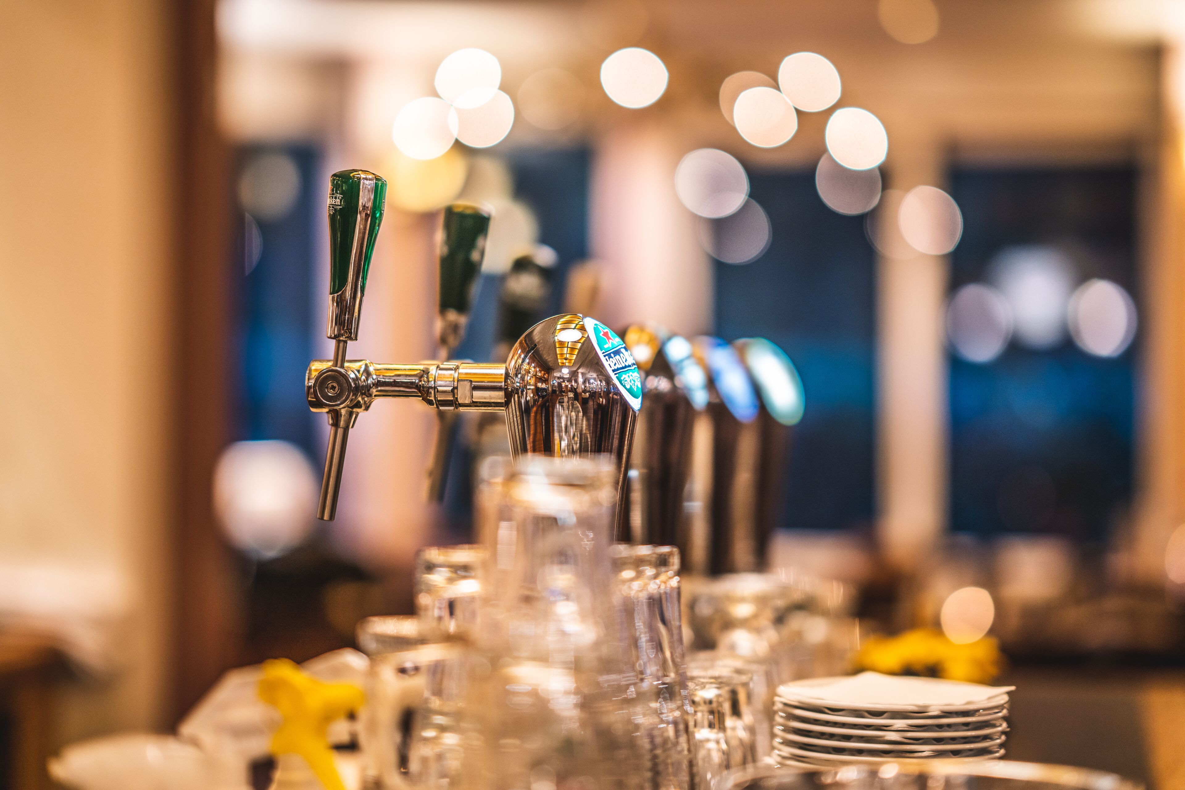 A row of beer taps with a blurred background of lights.